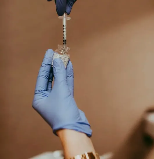Profissional com luvas preparando um injetável em ambiente clínico